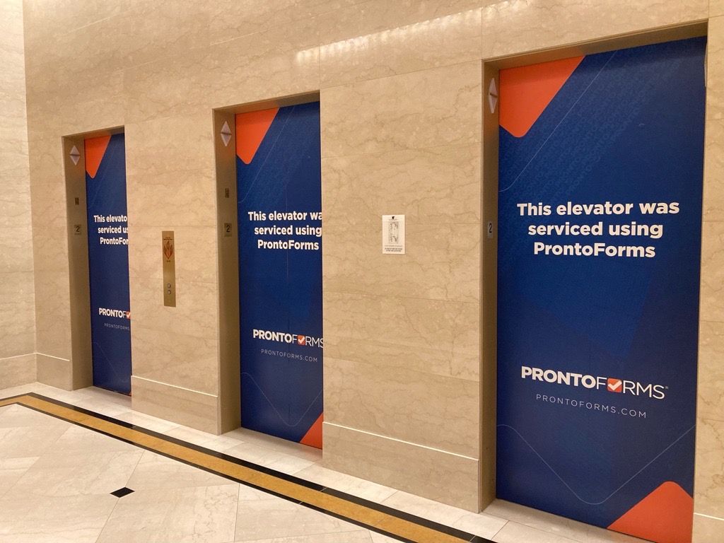 A bank of elevators at Service Council Symposium that read "This elevator was serviced using ProntoForms"